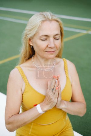 Foto de Mujer caucásica madura meditando al aire libre al atardecer en el campo de deportes. Mujer mayor meditando - Imagen libre de derechos