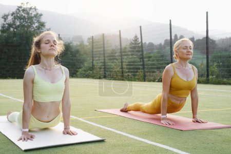 Photo for Two woman doing yoga outdoors Mother and adult daughter practicing together. Mature female and young girl having healthy activities. Family Active lifestyle and strength training in mountains - Royalty Free Image