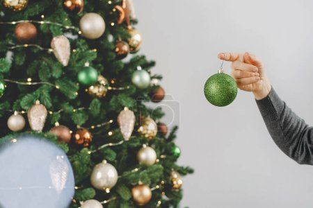 Foto de Mujer decorando un gran árbol de Navidad. Mujer de mediana edad sosteniendo bauble verde en la mano y colgando de la rama del árbol. Copiar espacio. Tarjeta de felicitación. Primer plano. - Imagen libre de derechos