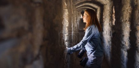 Téléchargez les photos : Bannière Femme marchant dans un vieux tunnel, regardant par la fenêtre. Château de visite féminin. Voyager dans un bâtiment ancien - en image libre de droit