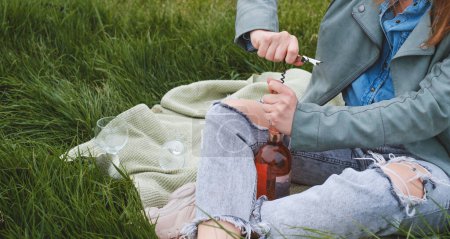 Téléchargez les photos : Bannière Femme dérouler la bouteille de vin rose sur le pique-nique. Belle femme mûre servir du vin en verre à l'extérieur sur l'herbe. Femme dans la cinquantaine dans le parc, gros plan - en image libre de droit