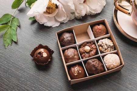 Téléchargez les photos : Bonbons au chocolat faits à la main dans la boîte sur la table noire. Chocolat aux noix et fruits secs et baies servi avec du café. - en image libre de droit