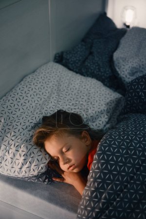 Photo for Child sleeping in bed at late night. Cute toddler girl pillow covered with warm blanket. Kid having night rest. Light on night table - Royalty Free Image