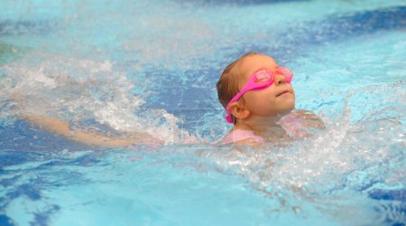 Foto de Buceo infantil en piscina. Niño pequeño saltando al agua con gafas aprendiendo a nadar. Chica divirtiéndose en el agua, salpicaduras en el parque acuático - Imagen libre de derechos