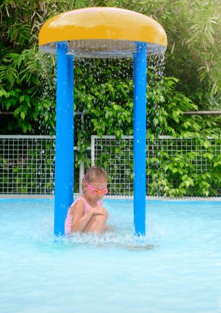 Téléchargez les photos : Petite fille se reposant dans la piscine dans l'aquapark intérieur. Heureux gisant dans l'eau avec des lunettes. Flux d'eau sur la tête des enfants - en image libre de droit