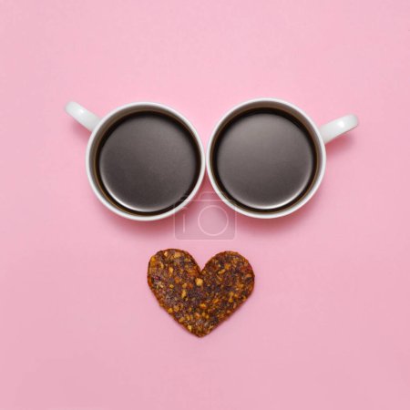 Photo for Coffee creative love emoji. Smile from two cups of black espresso and healthy raw heart shaped cookie as mouth. Smiley face with eyes on pink background. Top view. Valentines day positive emotions - Royalty Free Image
