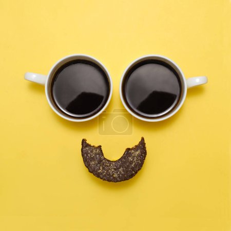 Foto de Café creativo emoji feliz. Sonríe desde dos tazas de espresso negro y un saludable donat crudo como boca. Cara sonriente con ojos sobre fondo amarillo. Vista superior. Comida que trae emociones positivas - Imagen libre de derechos