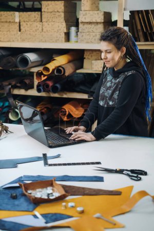 Photo for Online ordering tailoring from seamstress. Young woman business owner looking at laptop screen at tailoring manufactory. Fashion designer, tailor concept, leather and fabrics production. Upcycling - Royalty Free Image