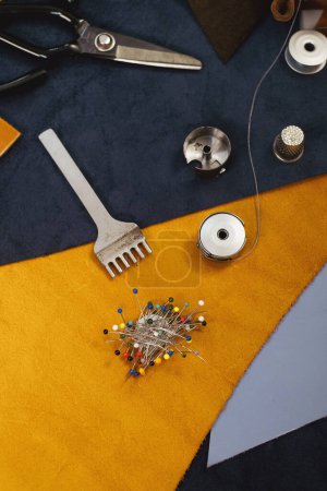 Photo for Tailor workplace accessories. Close up view of the eco leather and sewing equipment laying on the table. Set of pins, bobbin for a sewing machine, spool of thread, top view - Royalty Free Image