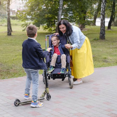 Photo for Family with child that has cerebral palsy, wheelchair user walking outdoors. Integration and accessibility of people with limited abilities, inclusion. Brother having illness - Royalty Free Image
