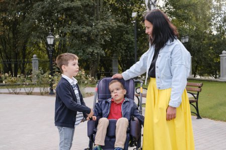Foto de Familia con niño que tiene parálisis cerebral, usuario de silla de ruedas que camina al aire libre. Integración y accesibilidad de personas con capacidades limitadas, inclusión. Hermano enfermo - Imagen libre de derechos