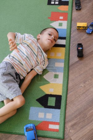 Téléchargez les photos : Enfant atteint de paralysie cérébrale jouant sur le tapis, s'amusant. Enfant ayant un trouble physique et mental jeux sensoriels et thérapie à la maison sur le sol. Handicap garçon avec limitations. Espace de copie - en image libre de droit