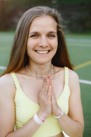 Téléchargez les photos : Femme souriante avec namaste après yoga en plein air pratique reconnaissante. Jeune femme à la vingtaine méditant - en image libre de droit