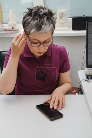Woman adjusting hearing aid through smartphone. Hearing loss treatment and small device for correction. Telehealth. heathy care, Manage hearing aid settings via smartphone Problem to hear.