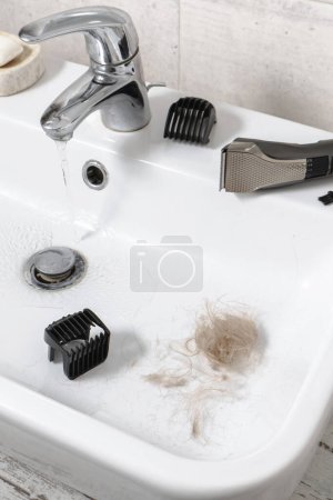 Téléchargez les photos : Rasoir électronique de nettoyage dans l'évier, soins personnels masculins et hygiène personnelle Vue de dessus. Cheveux dans l'évier. Cheveux longs blonds, machine - en image libre de droit