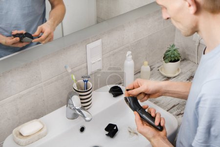 Téléchargez les photos : Rasoir électronique de nettoyage pour homme dans l'évier, soins personnels masculins et hygiène personnelle Vue de dessus. Cheveux dans l'évier avec chat. Cheveux blonds longs, machine dans les mains - en image libre de droit