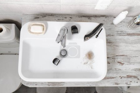 Foto de Limpieza afeitadora electrónica en fregadero, autocuidado masculino e higiene personal Vista superior. Cabello en el lavabo. Cabello largo y rubio, máquina - Imagen libre de derechos
