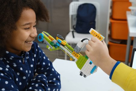 Classe de codage, écolière construisant un mécanisme de bras robotisé. enfants multiethniques faire de la science, tâches technologiques avec tablette. Éducation moderne afro-américaine fille avoir du plaisir à expérimenter sur la leçon