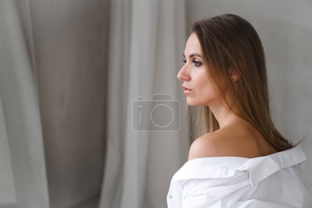 Téléchargez les photos : Jolie femme caucasienne douce heureuse en chemise blanche. Portrait audacieux de style de mode de femme sensuelle décisive. Confiante fille libre détendue, chambre ensoleillée du matin. Fraicheur, beauté, peau naturelle - en image libre de droit
