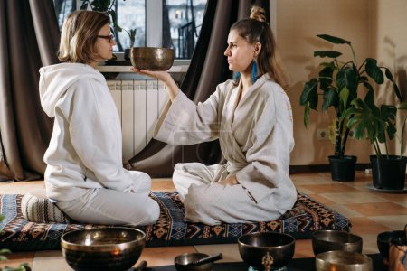 Sound healing with singing bowls, vibration massage and alternative therapy. Mental health care, meditation and relax. Therapist playing to old mature woman in 60s. singing, meditating practice