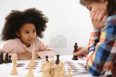 Téléchargez les photos : Groupe diversifié d'enfants jouant aux échecs. Enfants intelligents multiethniques concentrés avec jeu de société s'amusant à l'école. afro-américaine fille et caucasiens garçons sur échecs leçon stratégie - en image libre de droit