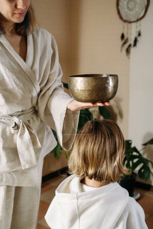 headache Sound healing with singing bowls, vibration massage and alternative therapy. Mental health care, meditation relax. Therapist playing to old mature woman in 60s. singing meditating practice
