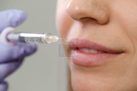 Photo for Lips augmentation injections for attractive woman. Plastic surgeon does injection in lip in medical clinic. Cosmetic rejuvenating facial treatment. Close-up - Royalty Free Image
