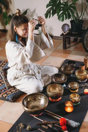 Sound healing with singing bowls, vibration massage and alternative therapy. Mental health care in green atmospheric studio. Woman playing to karatala instrument. taal, manjira clash cymbals