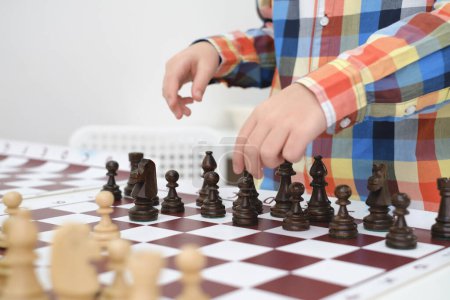 Foto de Primer plano de mano chico caucásico jugando ajedrez. Feliz niño concentrado detrás del ajedrez en clase o clase escolar. Emocionado niño inteligente escuela primaria con primer plano juego de mesa - Imagen libre de derechos