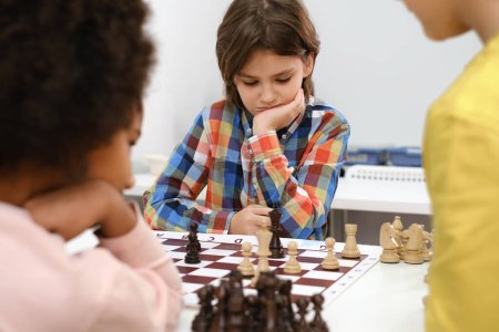 Téléchargez les photos : Groupe diversifié d'enfants jouant aux échecs. Enfants intelligents multiethniques concentrés avec jeu de société s'amusant à l'école. afro-américaine fille et caucasiens garçons sur échecs leçon stratégie - en image libre de droit