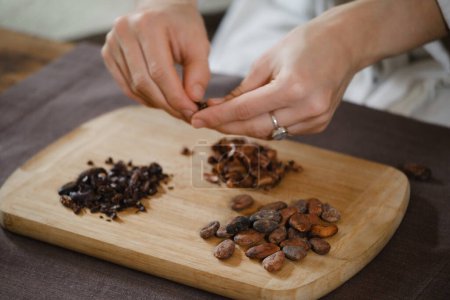 Foto de Manos pelando granos de cacao orgánicos en la mesa de madera, plumas de cacao, fabricación de chocolate artesanal en estilo rústico para la ceremonia en la mesa. Degustación, primer plano - Imagen libre de derechos