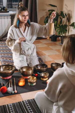Photo for Sound healing with singing bowls, vibration massage and alternative therapy. Mental health care in green atmospheric studio. Woman playing to percussion instrument. singing along, meditating music - Royalty Free Image