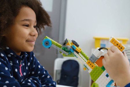 Classe de codage, écolière construisant un mécanisme de bras robotisé. enfants multiethniques faire de la science, tâches technologiques avec tablette. Éducation moderne afro-américaine fille avoir du plaisir à expérimenter sur la leçon