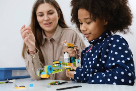 Coding Class, school girl constructing robot arm mechanism. multiethnic children making science, technology tasks with tablet. Modern education African American girl having fun experimenting on lesson