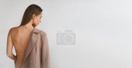 Téléchargez les photos : Bannière Jolie femme caucasienne effrontée détachant sa veste d'affaires. Sensuel corps de style de mode de femme forte décisive dans la pièce minimaliste. Dos nu, épaule couverte d'une veste. Espace de copie - en image libre de droit