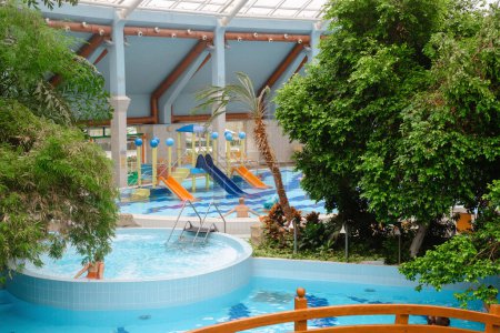 Wasserfontäne im Aquapark. Pilzförmiger Brunnen im Indoor-Erlebnispark voller grüner Palmen mit Brücke und Swimmingpools, Whirlpools im Innenbereich