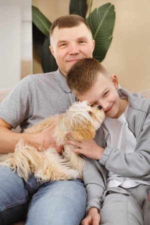 Téléchargez les photos : Homme et garçon assis sur le canapé avec un chien, relaxant à l'intérieur en famille. - en image libre de droit