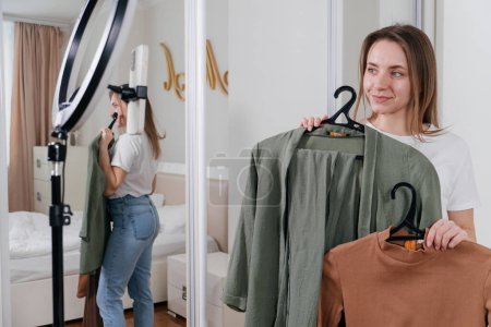 Photo for Female Blogger Recording Vlog Video on smartphone At Home Online Influencer On near bed choosing clothes, earthly look - Royalty Free Image