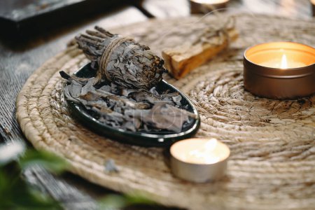 Photo for Woman hands burning white sage, before ritual on the table with candles and green plants. Smoke of smudging treats pain and stress, clear negative energy and meditation - Royalty Free Image