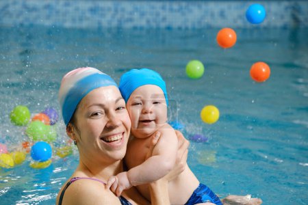 Early swimming coach training to swim baby boy in indoor pool. Playing activity for infant with mother, child physical development in water with joy and fun. Accessories and toys for diving lesson