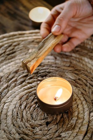 Téléchargez les photos : Femme mains brûlant Palo Santo, avant rituel sur la table avec des bougies et des plantes vertes. La fumée de la purification traite la douleur et le stress, élimine l'énergie négative et le bâton de bois de méditation - en image libre de droit