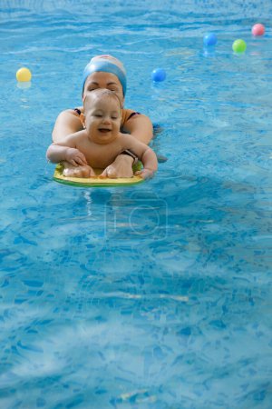 Téléchargez les photos : Early age swimming in pool. Baby kid trained to swim in water. Happy child with coach woman in indoor swimming pool playing and having fun. Healthy and sport family with infant, active family - en image libre de droit