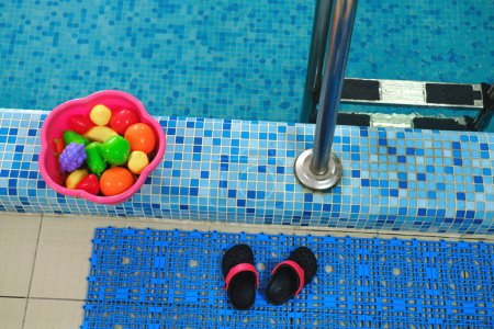 Photo for Empty indoors public swimming pool for kids. sports balls. children center, pool with children equipment. Flip flops near side - Royalty Free Image