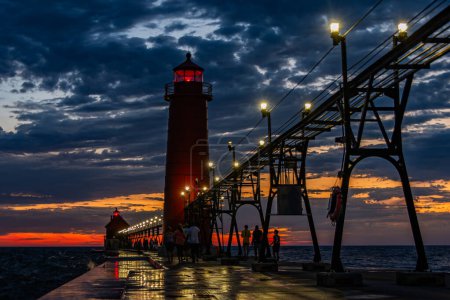A sunset and storm clouds create dramatic lighting behind Grand Haven, Michigan lighthouse and pier. High quality photo