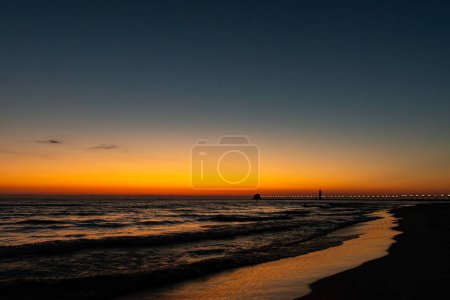 A golden horizon fades to deep blue sky as the sun sets over Lake Michigan at Grand Haven, Michigan. High quality photo