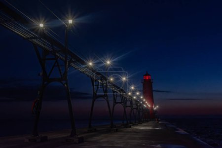 Lichter erleuchten Grand Haven, Michigan, Pier und Leuchtturm, während der Himmel dunkelblau wird. Hochwertiges Foto