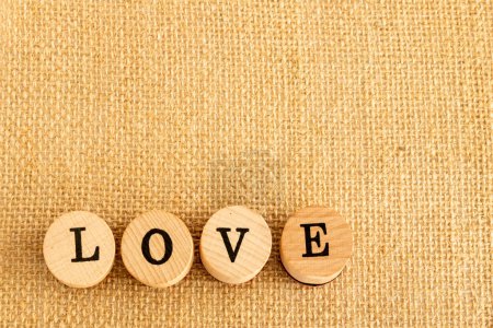 Téléchargez les photos : Morceaux ronds de bois qui forment le mot Love en noir sur un fond de jute marron - en image libre de droit