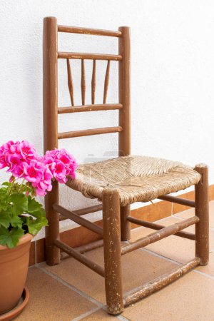 Téléchargez les photos : Petite chaise antique avec géranium rose avec fond mural blanc - en image libre de droit