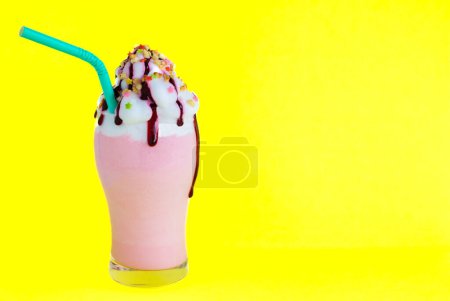 Téléchargez les photos : Milkshake aux fraises avec crème, sirop de fraise, amandes grillées, étoiles de bonbons colorées, tube en carton vert sur fond jaune vif, avec zone de copie, espace de copie. - en image libre de droit