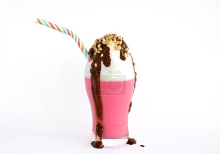 Téléchargez les photos : Milkshake aux fraises, crème, morceaux d'amande et chocolat se répandant hors du verre sur un fond blanc - en image libre de droit